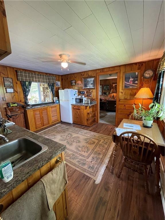 kitchen with sink, wooden walls, wood-type flooring, ceiling fan, and white refrigerator