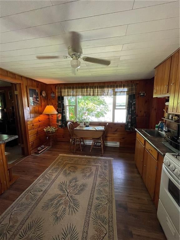 kitchen with sink, dark hardwood / wood-style flooring, white range with electric stovetop, wooden walls, and ceiling fan