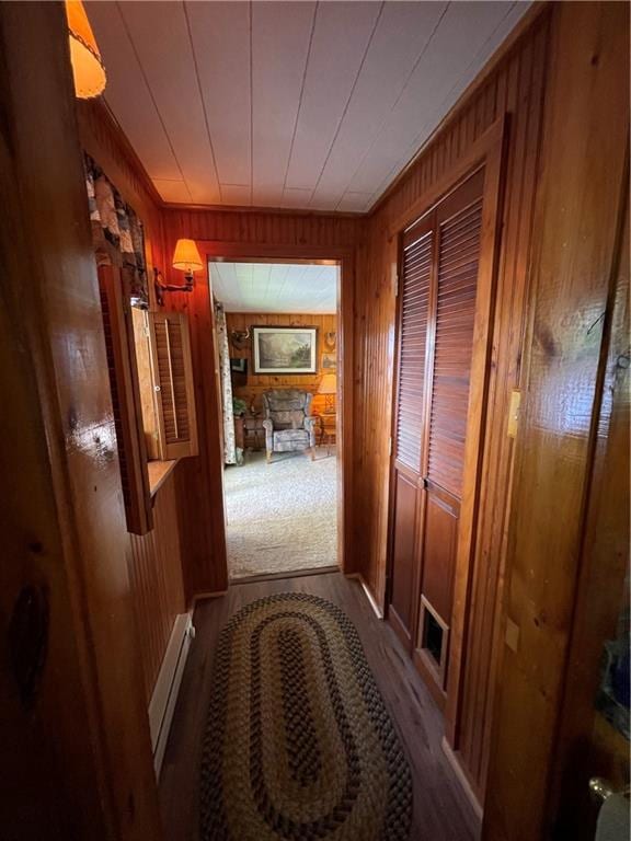 hall with carpet flooring, wooden walls, and a baseboard heating unit