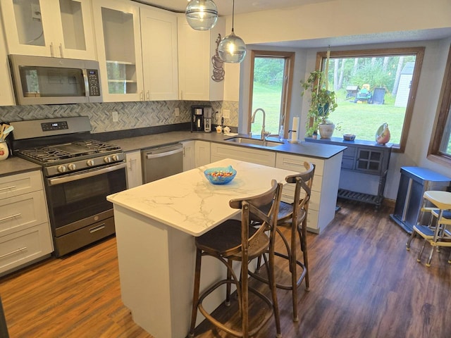 kitchen with sink, dark wood-type flooring, tasteful backsplash, stainless steel appliances, and pendant lighting