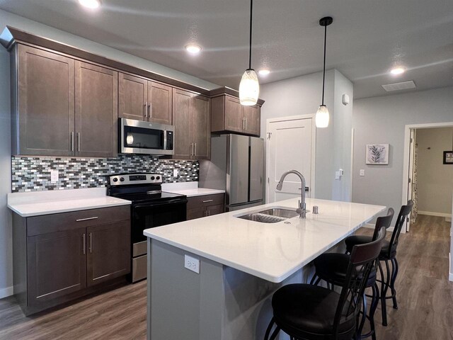 kitchen featuring appliances with stainless steel finishes, decorative light fixtures, decorative backsplash, hardwood / wood-style floors, and a center island with sink