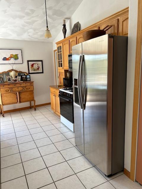 kitchen with range with gas stovetop, lofted ceiling, decorative light fixtures, light tile patterned floors, and stainless steel fridge with ice dispenser