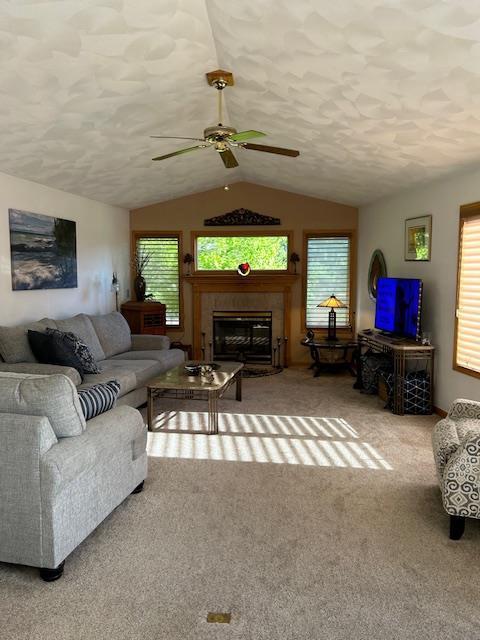 carpeted living room with a tile fireplace, vaulted ceiling, ceiling fan, and a textured ceiling