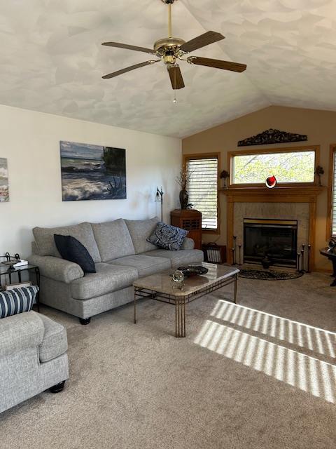 carpeted living room featuring a tile fireplace, vaulted ceiling, and ceiling fan