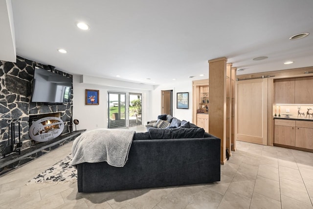 living room featuring a barn door, a stone fireplace, and light tile patterned floors