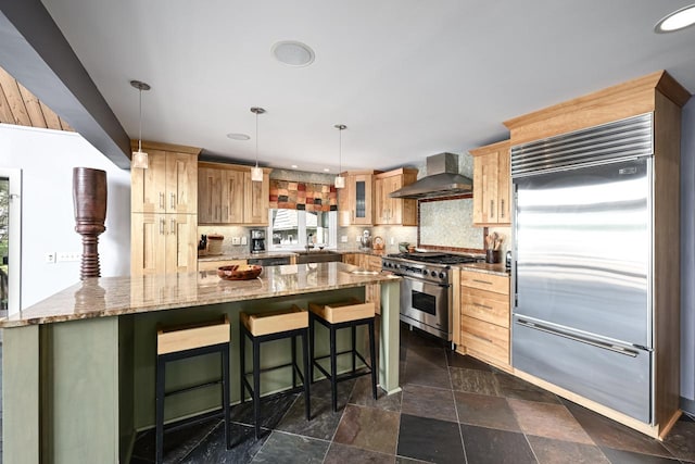 kitchen with decorative backsplash, a kitchen bar, wall chimney range hood, premium appliances, and hanging light fixtures