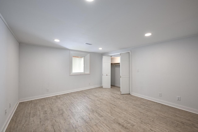 unfurnished bedroom with a walk in closet, a closet, light hardwood / wood-style flooring, and crown molding