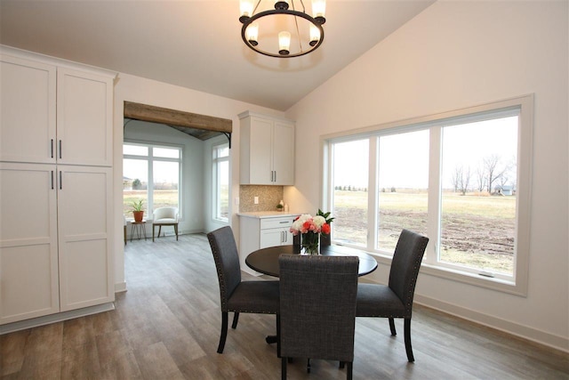 dining area featuring lofted ceiling, wood finished floors, baseboards, and a chandelier