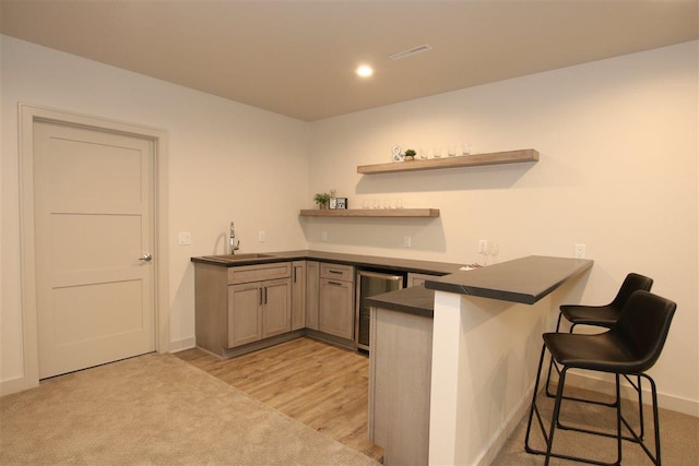 kitchen with a sink, a kitchen breakfast bar, dark countertops, wine cooler, and a peninsula