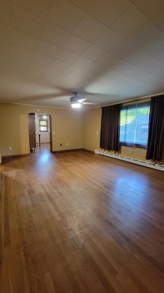 unfurnished room featuring arched walkways, baseboards, baseboard heating, and wood finished floors