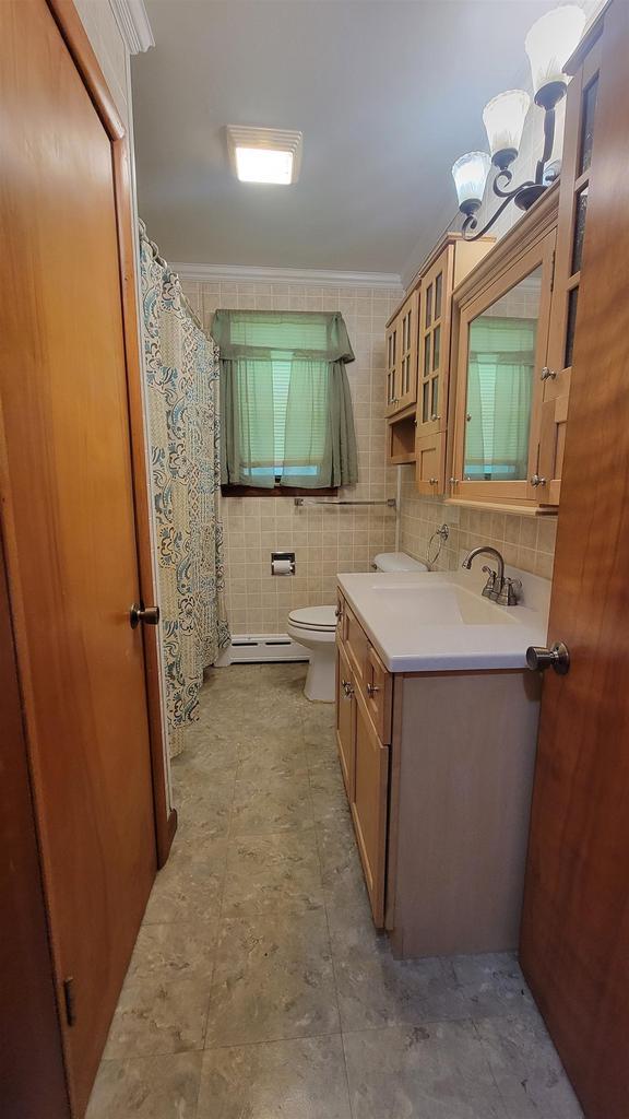 bathroom with a notable chandelier, tile walls, crown molding, toilet, and vanity