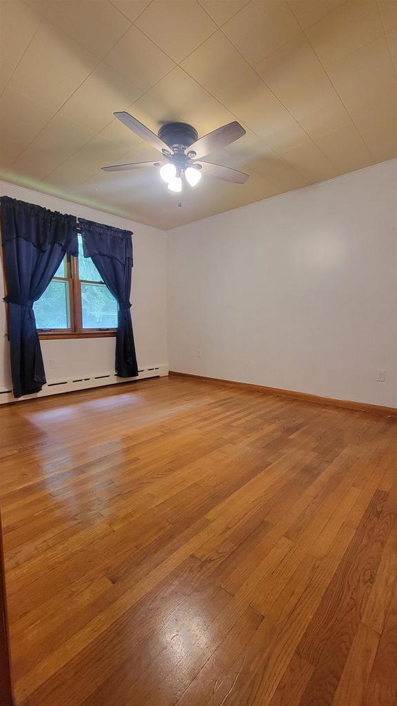 spare room with baseboards, ceiling fan, a baseboard heating unit, and light wood-style floors