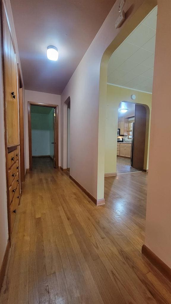 hallway featuring arched walkways, light wood-style flooring, and baseboards