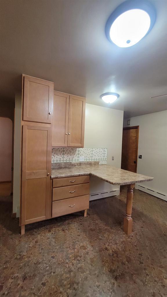 kitchen with a kitchen breakfast bar, kitchen peninsula, a baseboard radiator, and light brown cabinetry