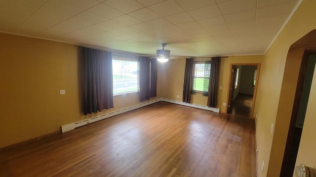 empty room with a healthy amount of sunlight, arched walkways, crown molding, and wood finished floors