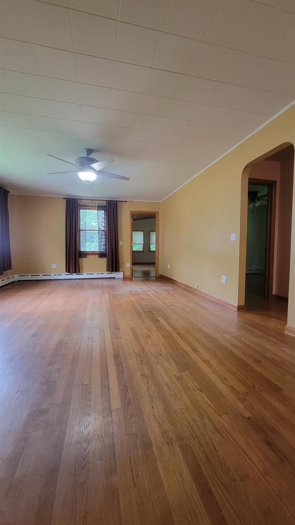 unfurnished living room with arched walkways, wood finished floors, a ceiling fan, and baseboards