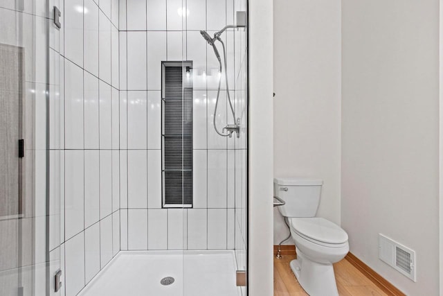 full bathroom with toilet, visible vents, wood finished floors, and tiled shower