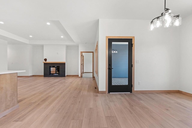 interior space with recessed lighting, a fireplace, baseboards, light wood-type flooring, and a raised ceiling