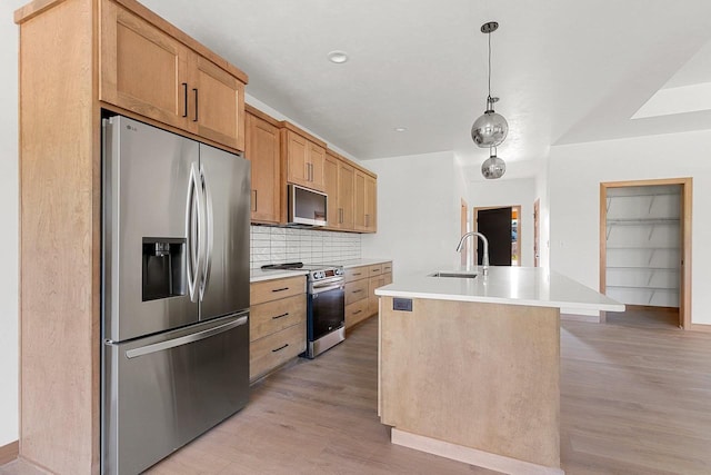 kitchen with appliances with stainless steel finishes, sink, an island with sink, hanging light fixtures, and light hardwood / wood-style flooring