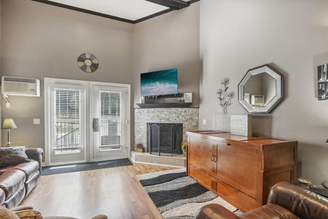 living room with a stone fireplace, wood finished floors, a towering ceiling, a wall mounted AC, and crown molding