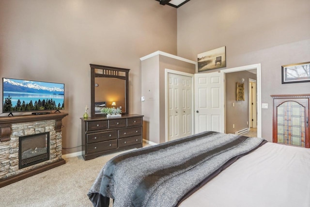 bedroom with baseboards, a high ceiling, baseboard heating, carpet flooring, and a stone fireplace