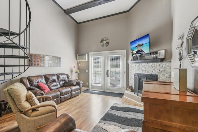 living room featuring stairway, wood finished floors, a high ceiling, an AC wall unit, and a stone fireplace