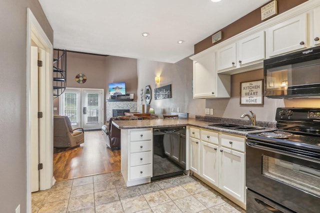 kitchen with white cabinetry, a sink, a stone fireplace, a peninsula, and black appliances