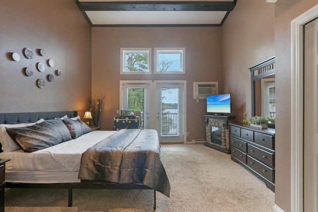 carpeted bedroom featuring a baseboard heating unit, access to exterior, a towering ceiling, and a stone fireplace