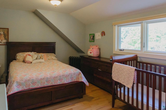 bedroom with light hardwood / wood-style flooring, vaulted ceiling, and radiator