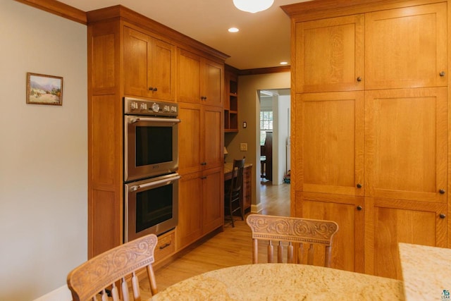 kitchen with light hardwood / wood-style flooring, stainless steel double oven, light stone counters, and ornamental molding