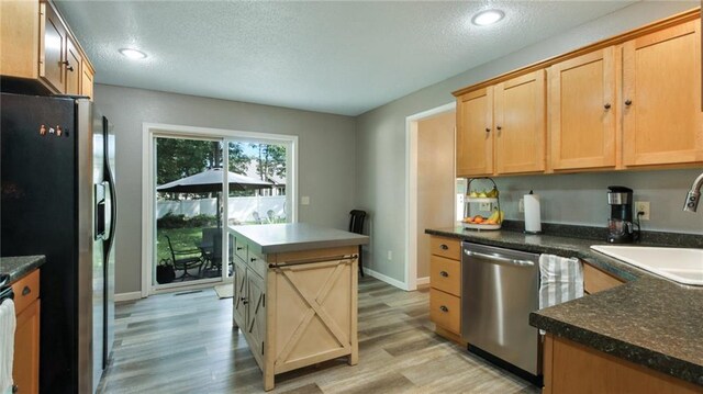 kitchen with a center island, stainless steel appliances, a sink, a textured ceiling, and light wood-type flooring