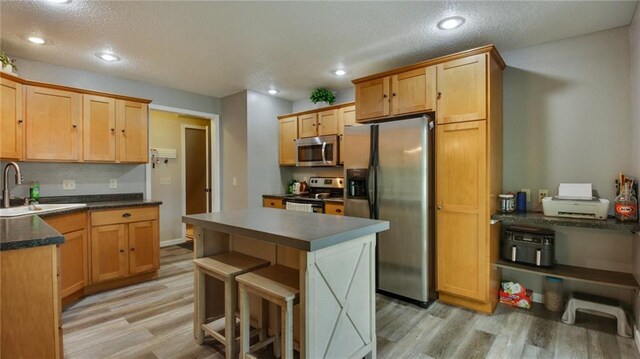 kitchen with recessed lighting, a sink, appliances with stainless steel finishes, light wood-type flooring, and dark countertops