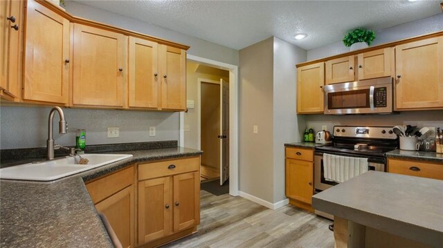 kitchen featuring appliances with stainless steel finishes, a textured ceiling, sink, and light wood-type flooring