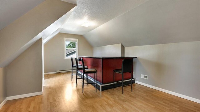 bonus room featuring baseboards, lofted ceiling, light wood-style flooring, baseboard heating, and a textured ceiling