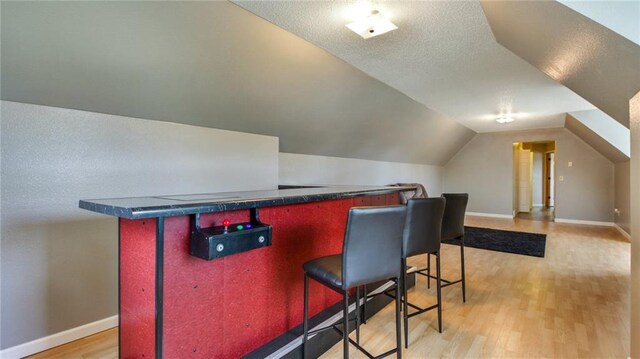 bonus room with light wood-type flooring, a textured ceiling, baseboard heating, and lofted ceiling