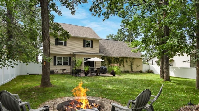 rear view of house with a shingled roof, a fenced backyard, a lawn, and a fire pit