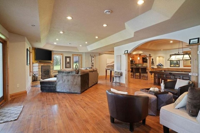 living room with a raised ceiling, light hardwood / wood-style flooring, and a stone fireplace