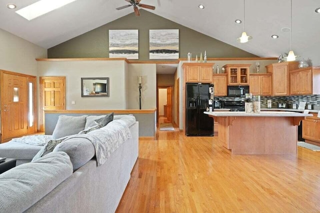 kitchen featuring high vaulted ceiling, light hardwood / wood-style flooring, a center island, and black appliances