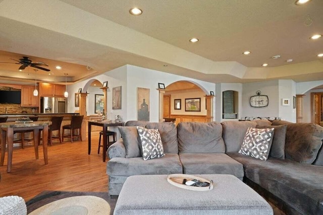 living room with ceiling fan, light hardwood / wood-style floors, and a raised ceiling