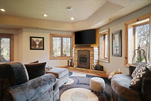 living room featuring a textured ceiling, a tray ceiling, and a stone fireplace