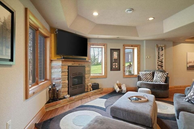 living room featuring hardwood / wood-style flooring, a textured ceiling, a tray ceiling, and a stone fireplace