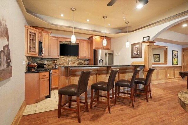 kitchen with light wood-type flooring, appliances with stainless steel finishes, ceiling fan, and a raised ceiling