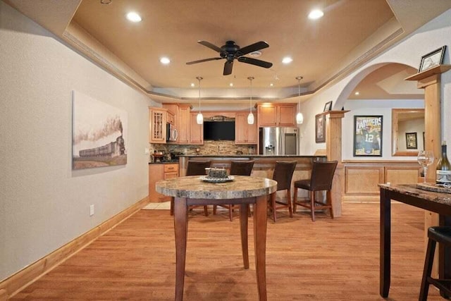 dining room with light hardwood / wood-style floors, ceiling fan, and a tray ceiling