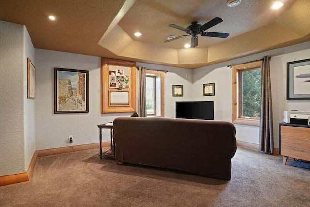 carpeted living room with ceiling fan, a textured ceiling, a tray ceiling, and a healthy amount of sunlight