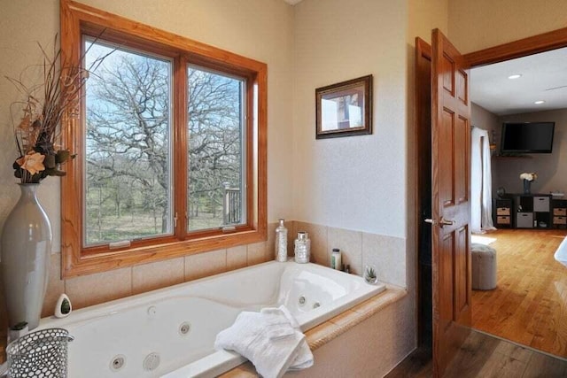 bathroom with a wealth of natural light, a relaxing tiled tub, and wood-type flooring