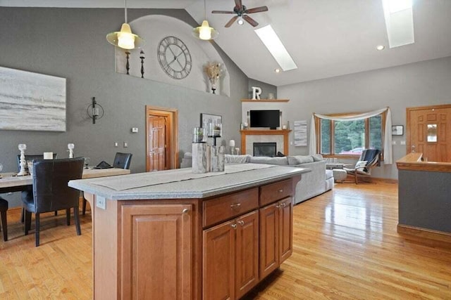 kitchen featuring light hardwood / wood-style flooring, a skylight, high vaulted ceiling, a kitchen island, and ceiling fan