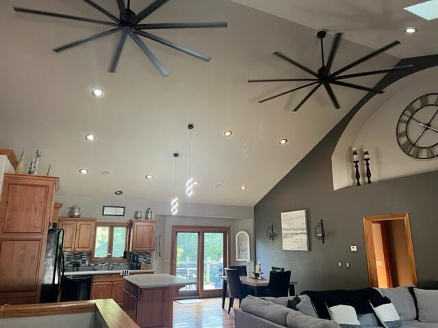 living room with sink, high vaulted ceiling, a skylight, and light hardwood / wood-style floors