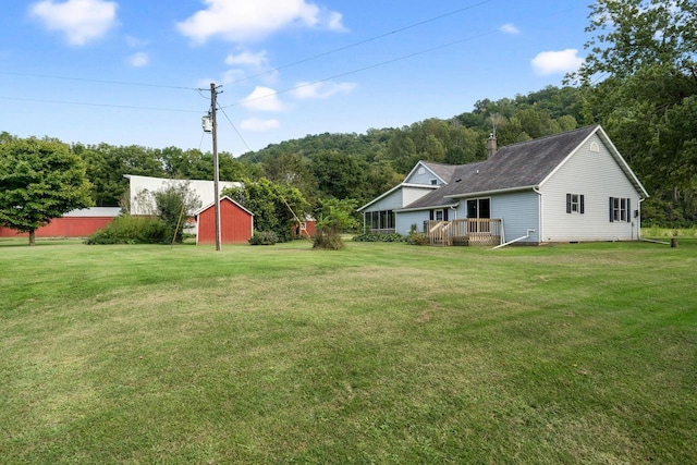 view of yard with an outdoor structure, a forest view, and a wooden deck