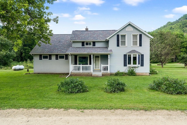 traditional-style house with a chimney, covered porch, a shingled roof, and a front lawn