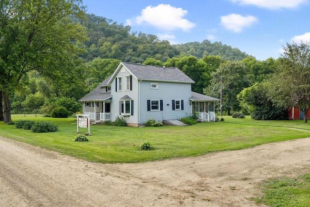 view of front of property featuring covered porch, a view of trees, a front lawn, and roof with shingles